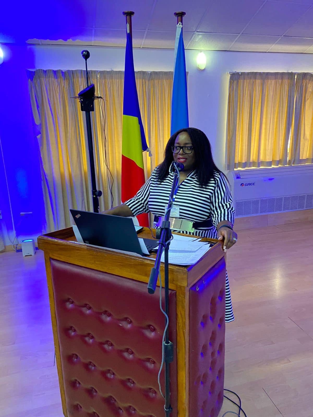 Vongai Nyahunzvi speaking from the podium at a United Nations convening, national and United Nations flags behind her.